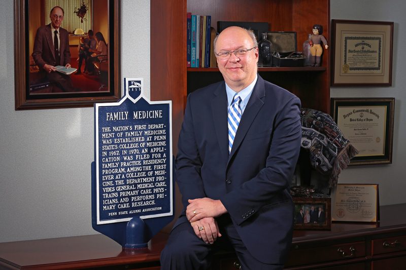 Mack Ruffin IV, MD, MPH, sits for a professional portrait next to an historical marker about the nation's first Department of Family Medicine being established at Penn State College of Medicine in 1967.