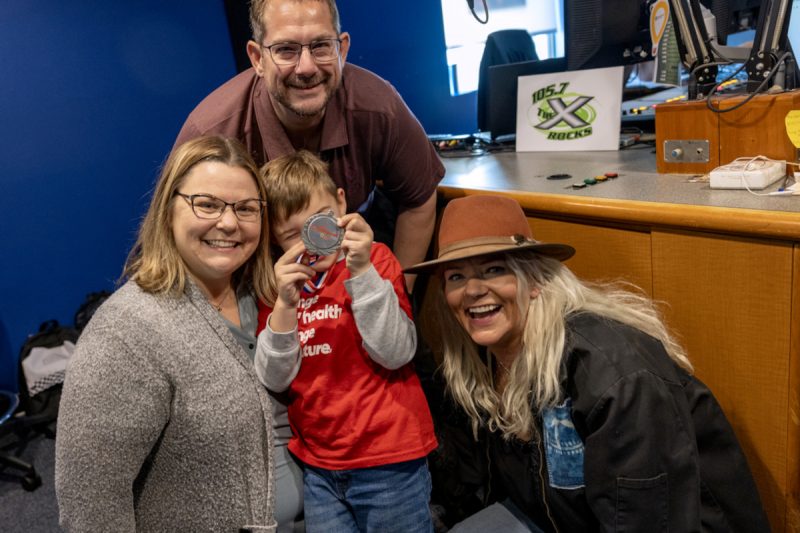 Three adults and one child pose for a photo in a radio studio, smiling.