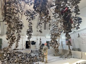 A U.S. soldier observes hundreds of worn boots hanging from the ceiling in the “Boots of Ali Al Salem” chandelier display