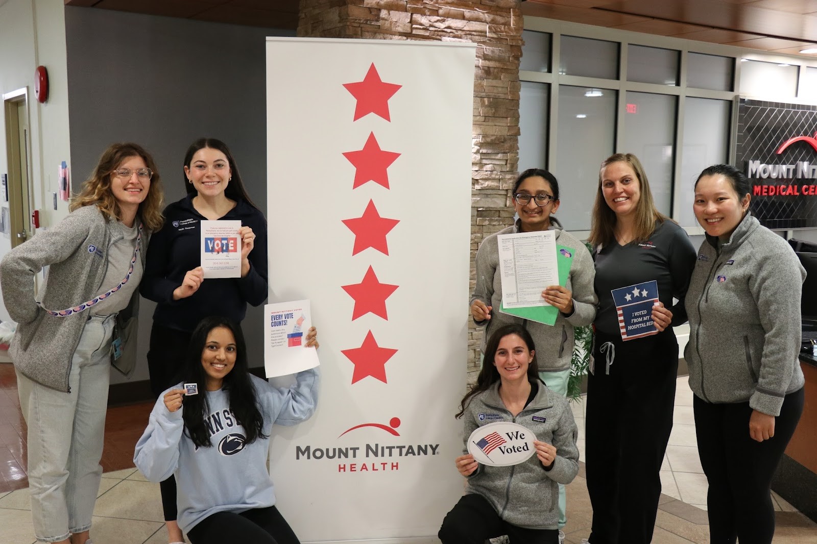 A group of seven people stands around a sign for Mount Nittany Medical Center.