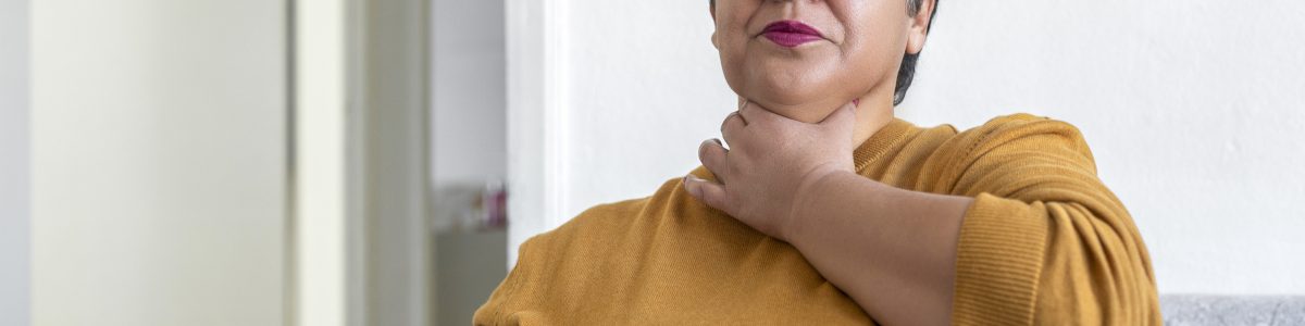 A woman suffering from acid reflux or heartburn holds her throat and closes her eyes.