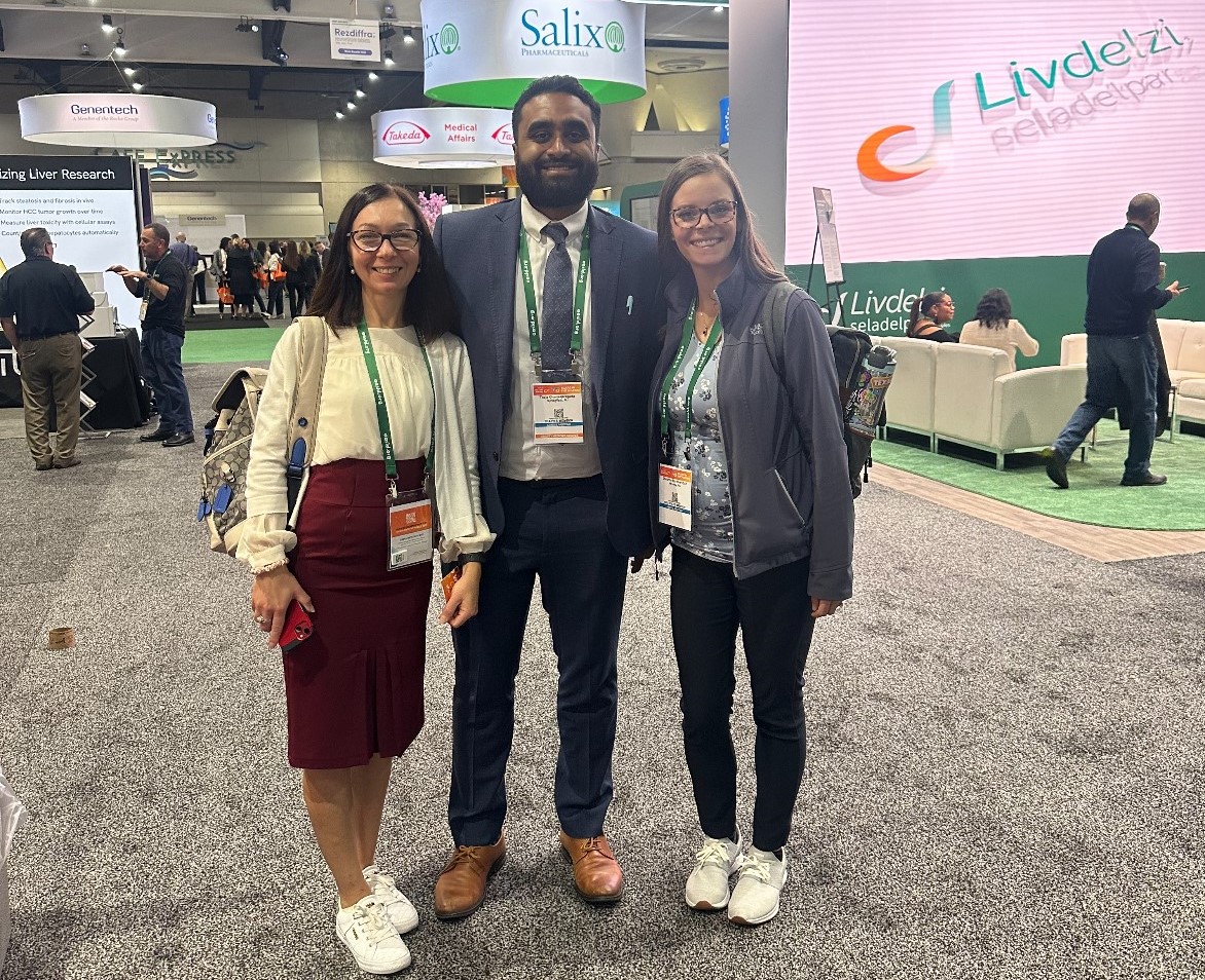 Dr. Nataliya Smith, Dr. Theja Channapragada and Breianna Hummer-Bair stand in the center of a conference center surrounded by exhibits.