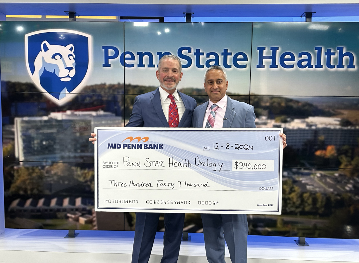 Two men in suits pose with a check made out to Penn State Health Urology for $340,000. A large Penn State Health logo sits in the background.