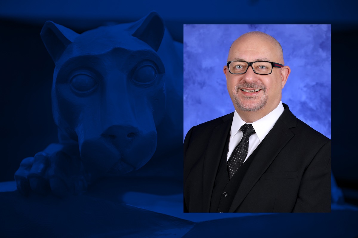 A headshot of a man smiling is overlaid on a blue background that has a statue of a lion mascot