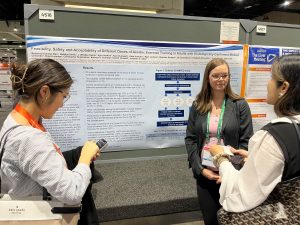 Breianna Hummer-Bair speaks with two individuals with a research poster displayed behind her.