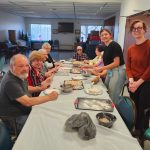 A group of older adults and medical students stands and sits at a table during a cooking class.