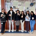 A group of six people stands together for a group photo with each person holding a cup of coffee.