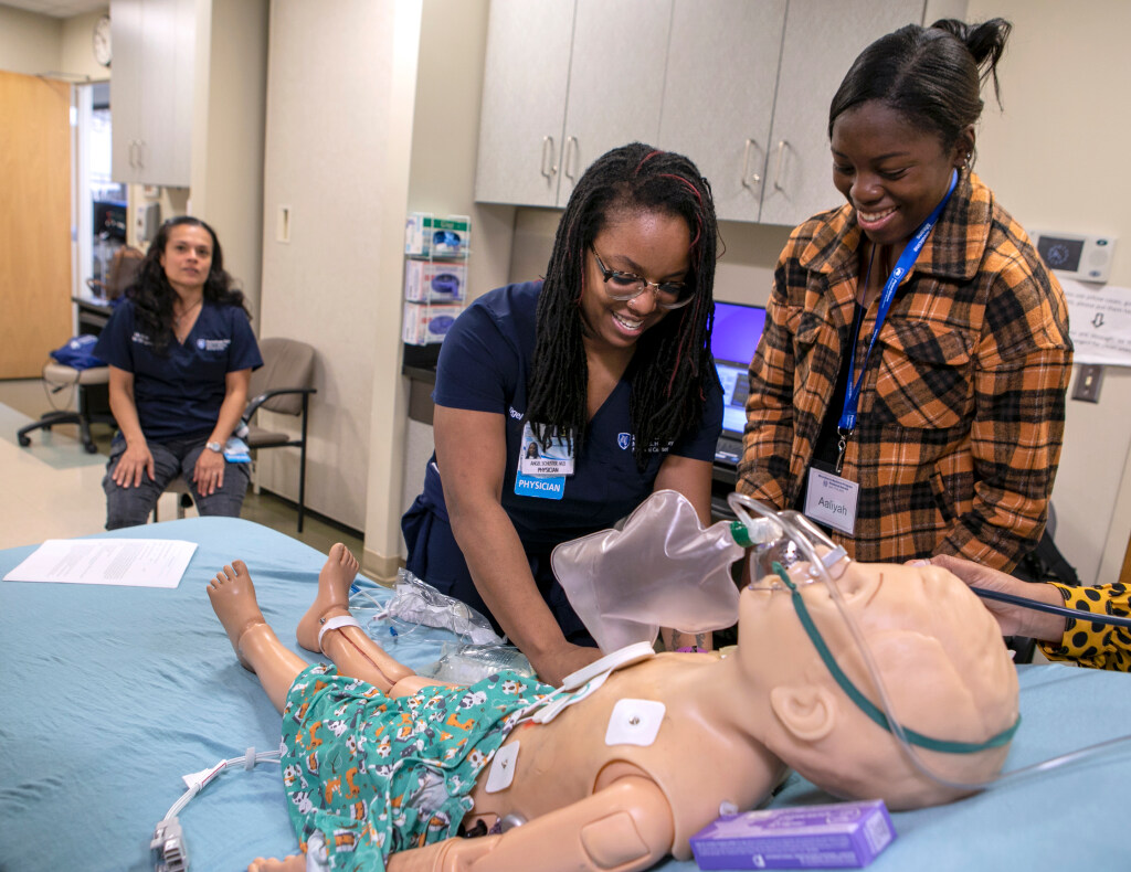Dr. Angel Schuster, center, touches a manikin in the Simulation Lab at Penn State College of Medicine in 2023 as a woman on the right watches. Another woman is seated on the left.
