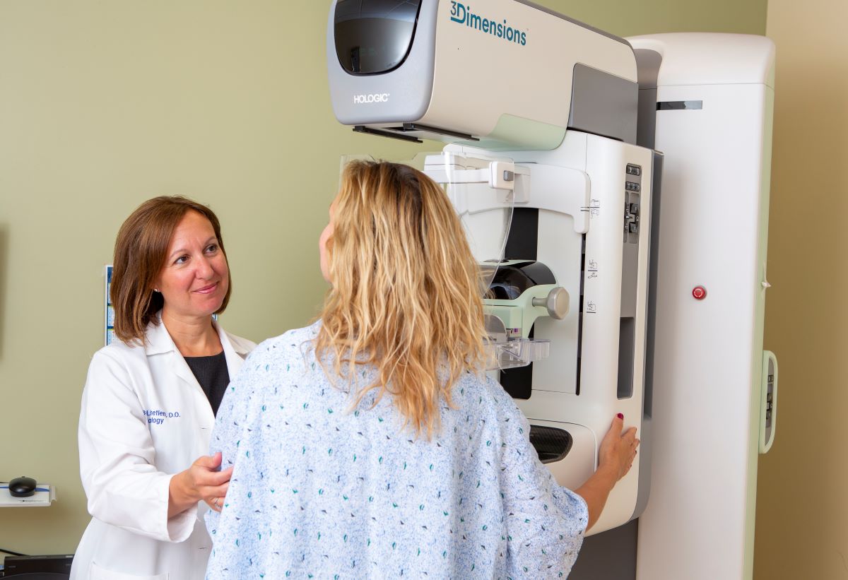 Dr. Alison Chetlen, left, touches a patient’s arm as she positions her in front of a mammography machine. Chetlen is wearing a white coat with her name and “Radiology” on the upper-right.