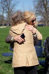Two women wearing outdoor coats embrace. Chairs are in the background.
