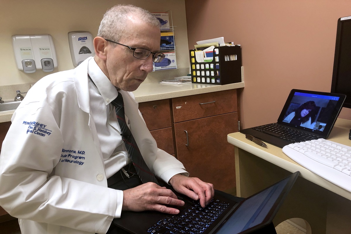 A doctor wearing a white coat types on a laptop.
