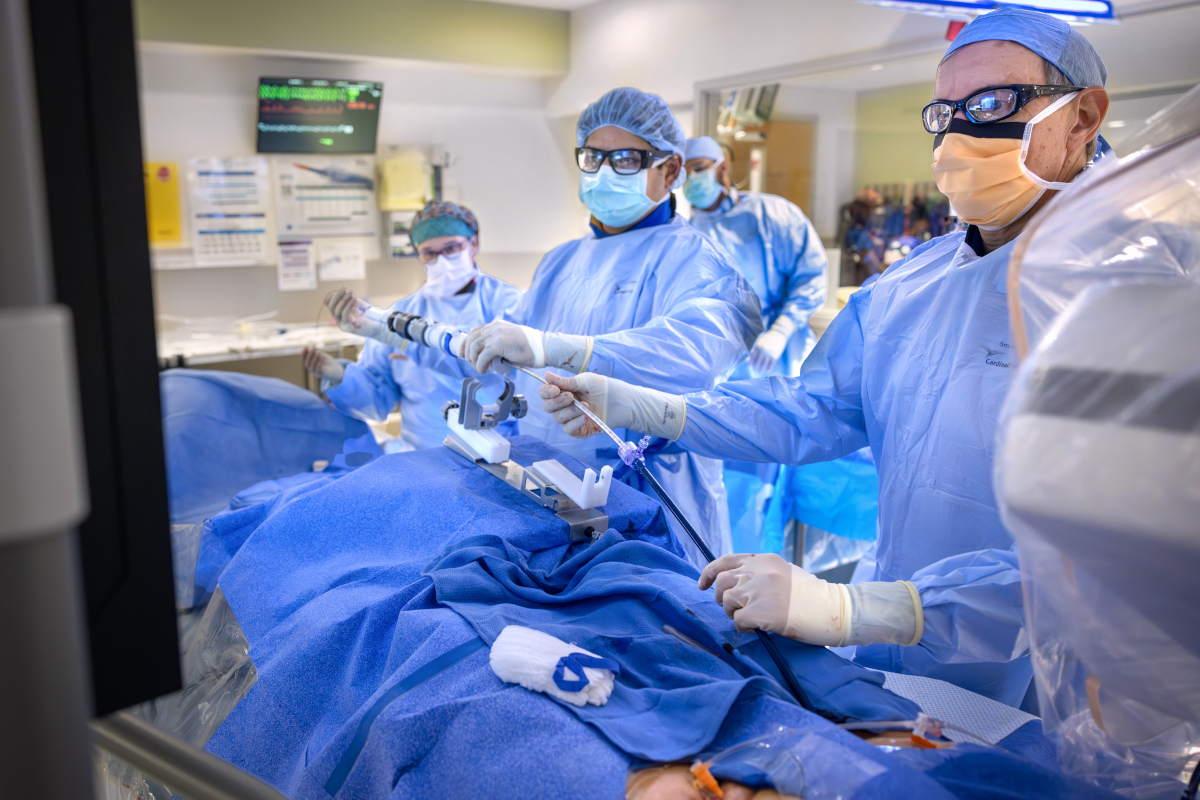A team of medical professionals in full surgical attire, including masks, gowns, and protective eyewear, performs a minimally invasive procedure in a hospital operating room.
