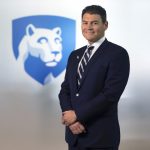 Dr. Michael Kupferman poses for a photo wearing a suit and tie. The Penn State Nittany Lion shield is in the background slightly out of focus.