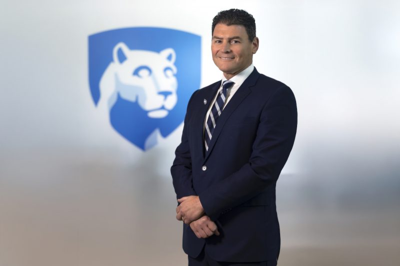 Dr. Michael Kupferman poses for a photo wearing a suit and tie. The Penn State Nittany Lion shield is in the background slightly out of focus.