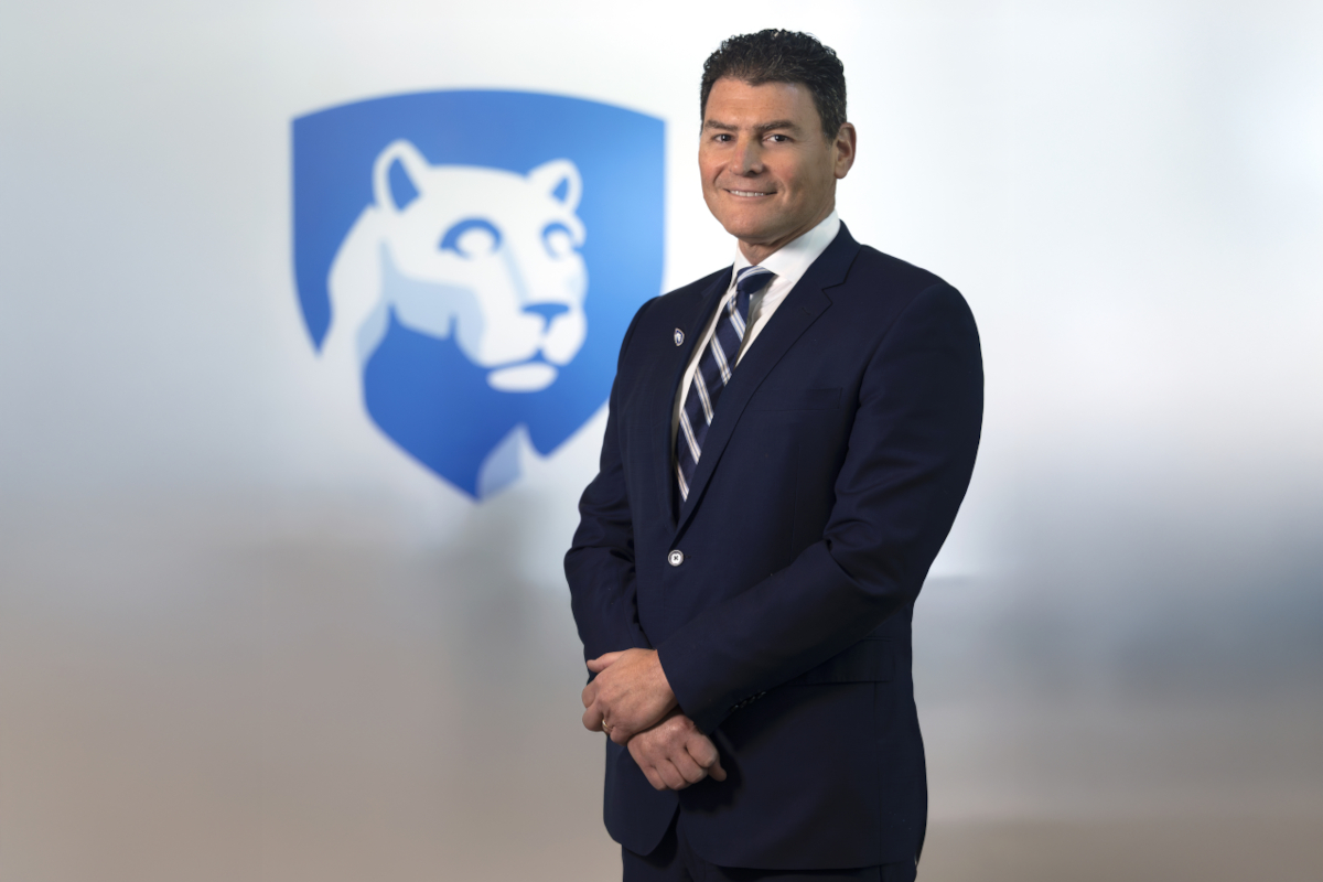 Dr. Michael Kupferman poses for a photo bearing a costume and a tie. The Penn Statenly's Shield Lion is in the background slightly out of development.