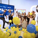 A group of excited children and adults celebrate on stage as blue and yellow balloons fall around them. Two WGAL 8 news anchors, one holding a baby, cheer in front of a large screen displaying a fundraising total of $343,054.00.