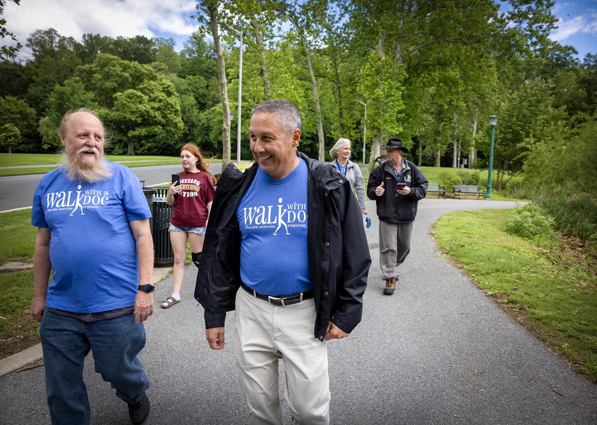 Two men wearing Walk With a Doc T-shirts smile as they walk at City Park in Reading. Behind them, three other people walk along the path.