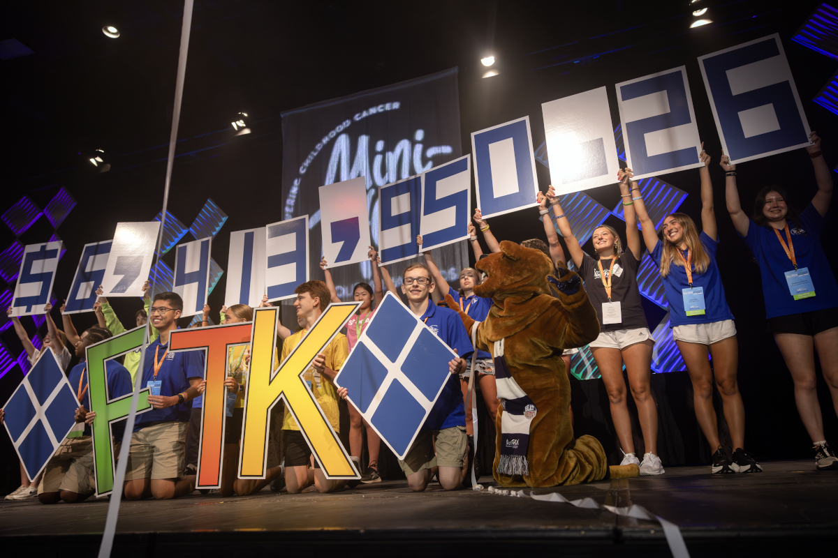 Several high school students, joined by the Nittany Lion, stand on stage and hold numbers - and the Four Diamonds logo - into the air.