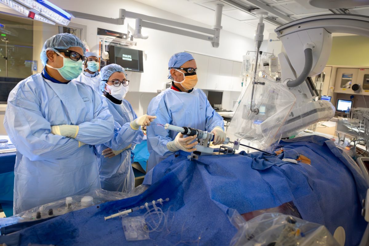 A medical team in full surgical attire, including masks, gowns, gloves, and protective eyewear, perform a procedure in a high-tech operating room.