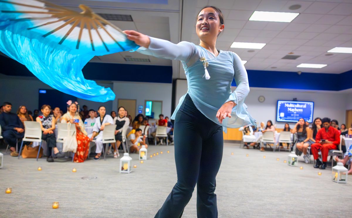 Sandy Zeng performs a Chinese fan dance, her outstretched arm holding a flourishing fan.