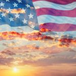 An American flag overlaid on a sunrise sky.