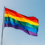 A rainbow LGBTQ+ pride flag flying with the sky in the background.