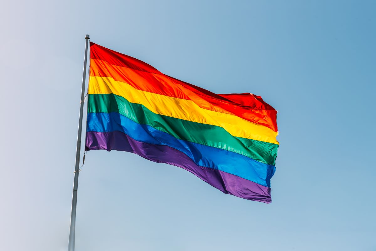 A rainbow LGBTQ+ pride flag flying with the sky in the background.