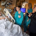 A woman lies in a hospital bed, holding a baby. A nurse speaks to the woman while the woman looks at another woman who is interpreting for her in sign language.