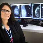 Radiologic technologist Erin Schaffner in her scrubs at Penn State Health Holy Spirit Medical Center. A mammogram scan is in the background on a computer screen.
