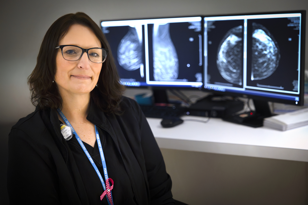 Radiologic technologist Erin Schaffner in her scrubs at Penn State Health Holy Spirit Medical Center. A mammogram scan is in the background on a computer screen.