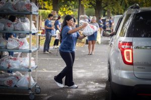 A student standing by a shelf of grocery bags hands one of the bags through a car window passing through the Cocoa Packs food distribution event.