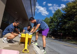 A group of three medical students stands around a children's wagon and cleans it.