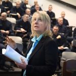 Terry Brosche of Penn State Health stands in front of a group of Pennsylvania State Police cadets who are sitting in an auditorium. She is gesturing, looking up and holding papers. She is wearing a suit jacket and blouse.