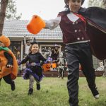 A group of children in Halloween costumes hold trick-or-treat buckets as they run in a backyard.