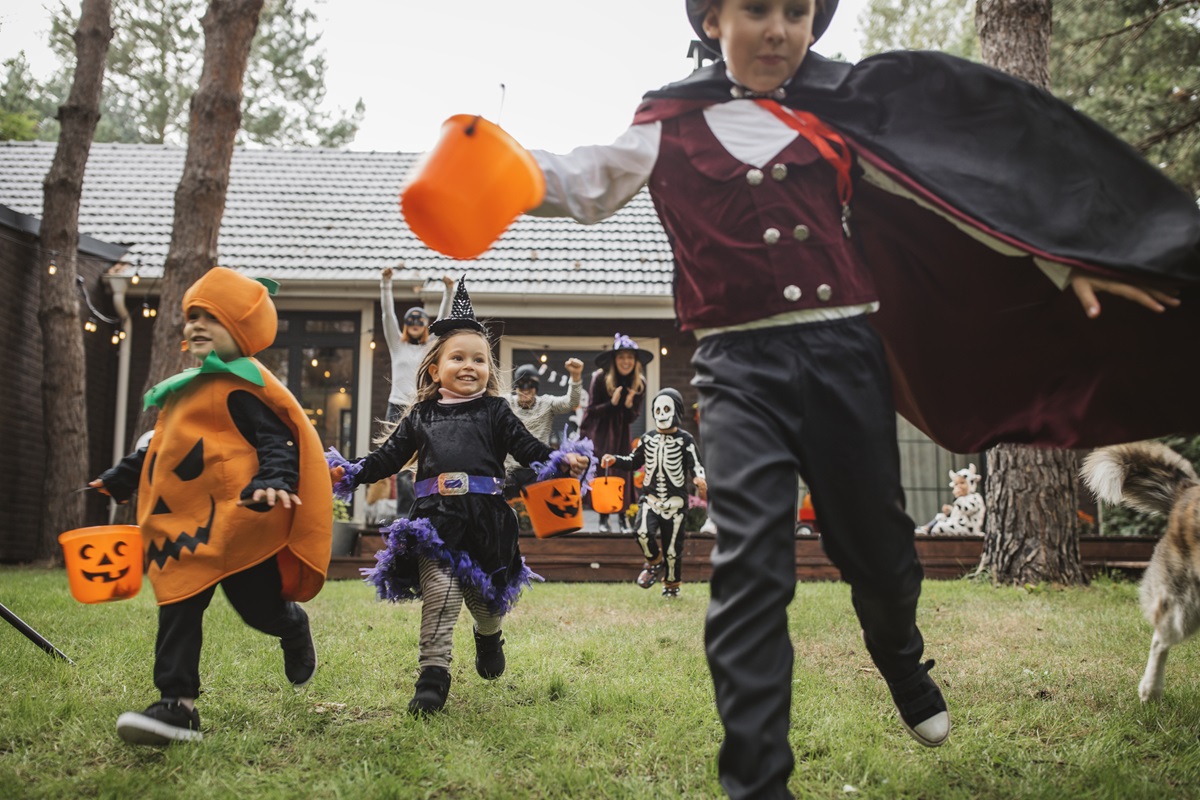A group of children in Halloween costumes hold trick-or-treat buckets as they run in a backyard.