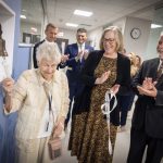 An older woman smiles as she rings a ceremonial bell mounted on the wall of the new Penn State Health Cancer Center at Hampden Medical Center.