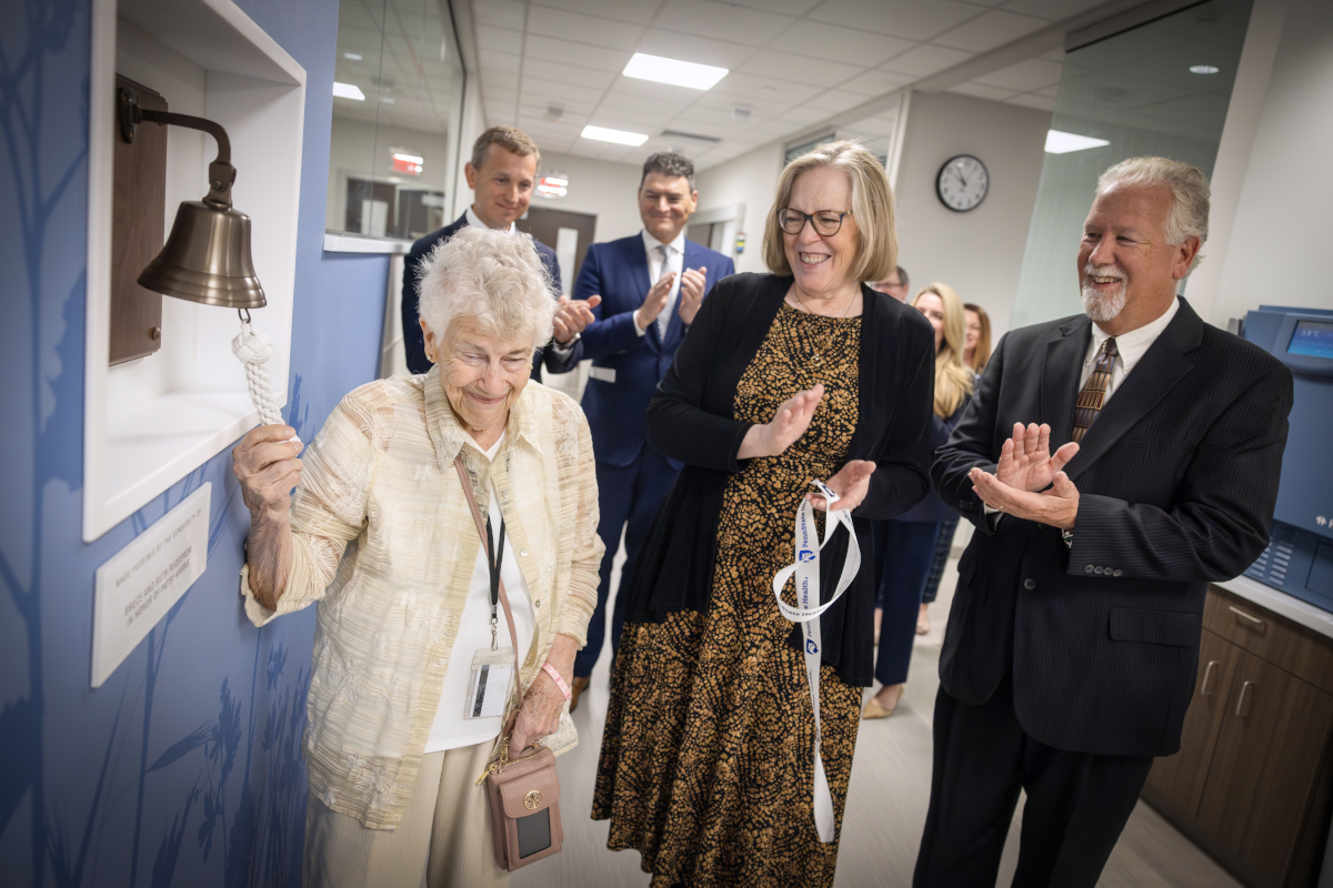 An older woman smiles as she rings a ceremonial bell mounted on the wall of the new Penn State Health Cancer Center at Hampden Medical Center.