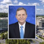 A professional headshot photo of Dr. Robert Harbaugh wearing a suit and tie is superimposed over an image of Milton S. Hershey Medical Center.