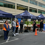 Three canopies branded Penn State Health Milton S. Hershey Medical Center a set up along the road in front of the medical center. Three hospital staff and three law enforcement officers stand under and around the canopies, facing the road.
