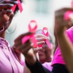 People standing together holding breast cancer ribbons.