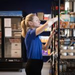 A person stacks grocery items on shelves.