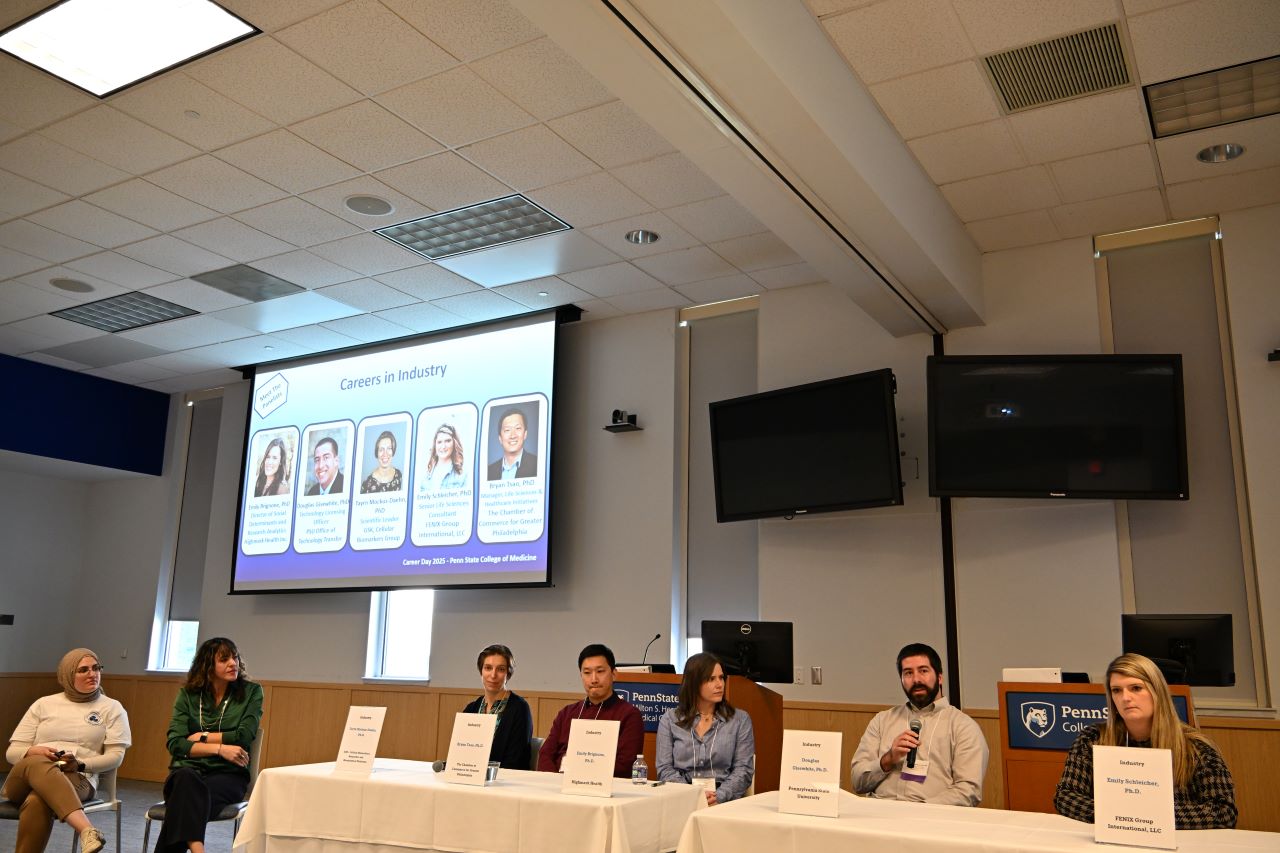 A group of individuals sits below a projector screen as they participate in a discussion panel.
