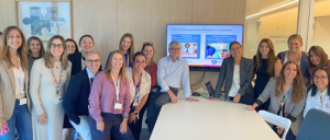 A large group of people gathers in a conference room around a table.