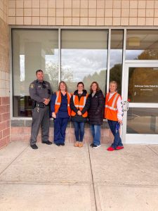 Five adults stand in a row outside a building entrance.