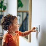 Toddler reaches into electrical outlet on wall with her hand.
