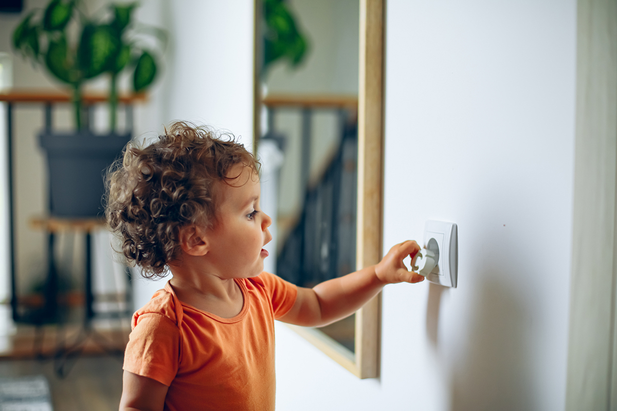 Toddler reaches into electrical outlet on wall with her hand.