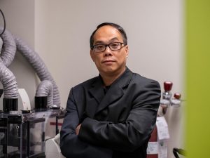 Pak Kin Wong, professor of biomedical engineering and mechanical engineering at Penn State, standing in a lab looking at a camera.