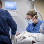 Two clinical team members tend to a patient who lays on a table of an MRI machine.