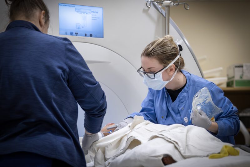Two clinical team members tend to a patient who lays on a table of an MRI machine.