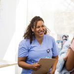 Smiling nurse and unrecognizable new mom talk about new baby.